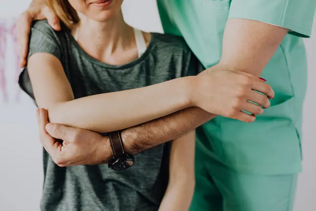 Crop anonymous chiropractor in uniform and wristwatch examining shoulder of smiling faceless woman in casual clothes in doctor office in clinic. Chiropractic practice hiring and training guide for 2027